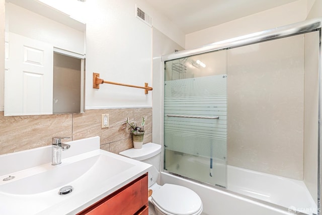 bathroom featuring tile walls, toilet, shower / bath combination with glass door, vanity, and tasteful backsplash