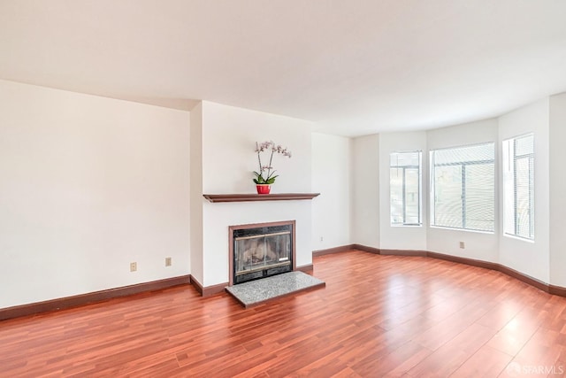 unfurnished living room with a glass covered fireplace, wood finished floors, and baseboards