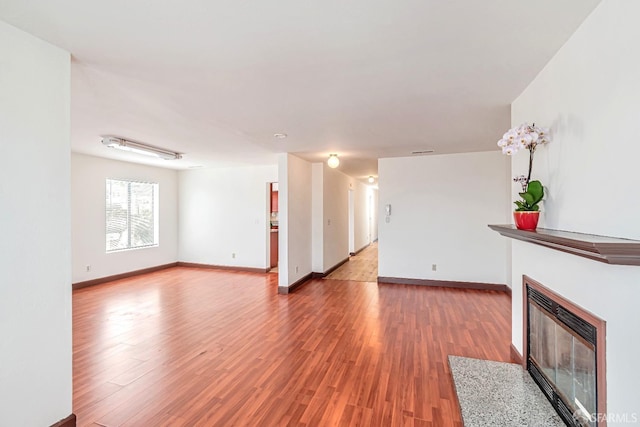 unfurnished living room with a fireplace with flush hearth, light wood-style floors, and baseboards