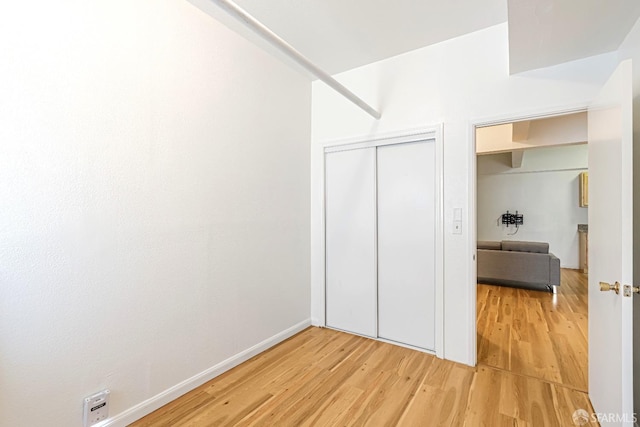 unfurnished bedroom featuring light wood-style flooring, a closet, and baseboards