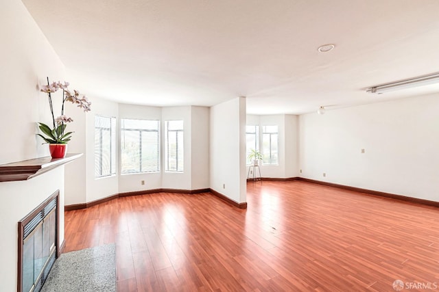 unfurnished living room featuring a glass covered fireplace, baseboards, and wood finished floors
