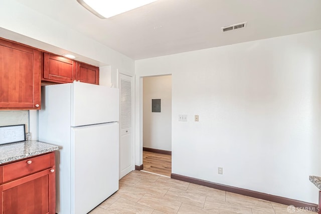 kitchen featuring freestanding refrigerator, light stone countertops, baseboards, and electric panel