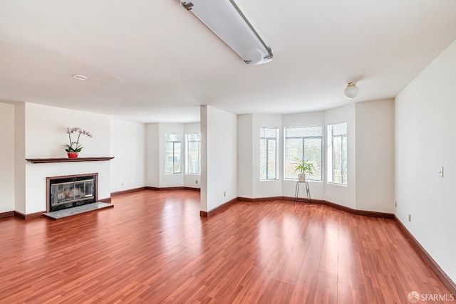 unfurnished living room featuring baseboards, wood finished floors, and a glass covered fireplace