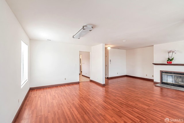 unfurnished living room with a glass covered fireplace, baseboards, and wood finished floors