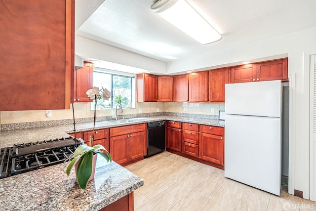 kitchen with freestanding refrigerator, black dishwasher, a sink, and light stone counters