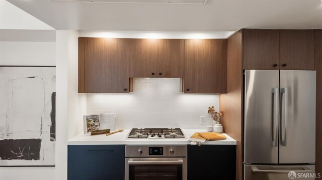 kitchen featuring light countertops, appliances with stainless steel finishes, brown cabinetry, and tasteful backsplash