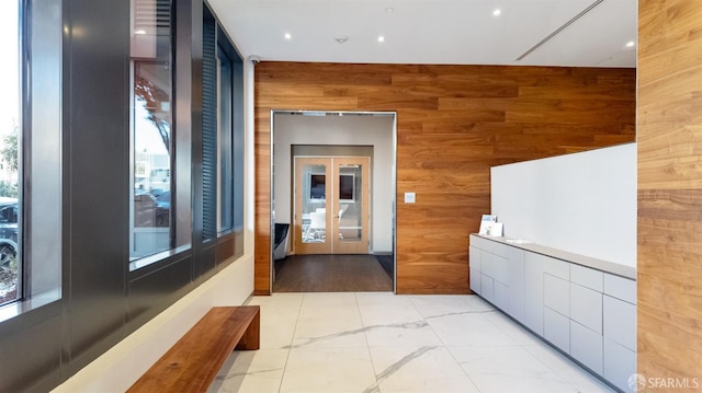 corridor with marble finish floor, wood walls, and french doors