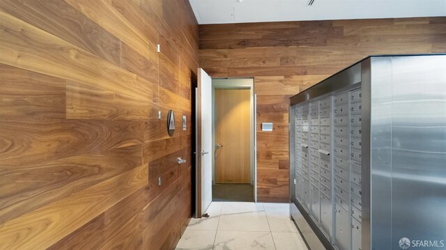 hall with marble finish floor, mail area, and wooden walls