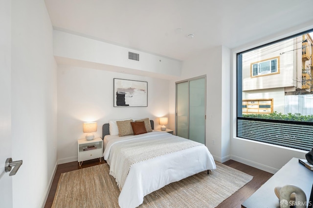 bedroom with a closet, wood finished floors, visible vents, and baseboards