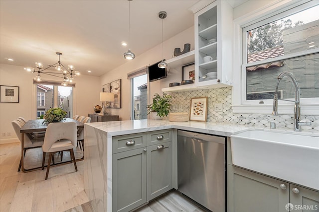 kitchen featuring light stone counters, gray cabinetry, stainless steel dishwasher, pendant lighting, and a sink