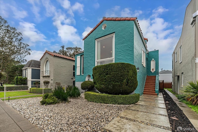 view of front facade with a tile roof, fence, and stucco siding