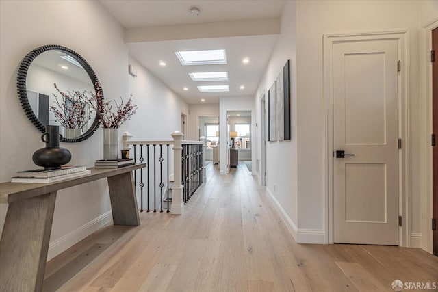 corridor featuring light wood-type flooring, recessed lighting, a skylight, and baseboards