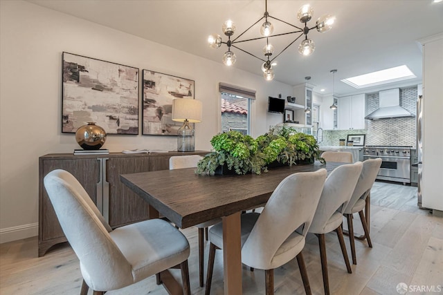 dining room featuring a skylight, light wood-style flooring, and baseboards