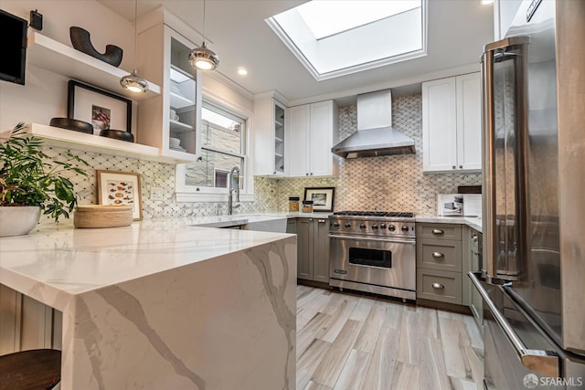 kitchen with premium appliances, white cabinets, hanging light fixtures, and wall chimney range hood