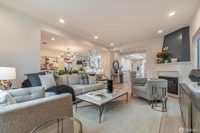 living area featuring light wood finished floors, recessed lighting, visible vents, an inviting chandelier, and a glass covered fireplace