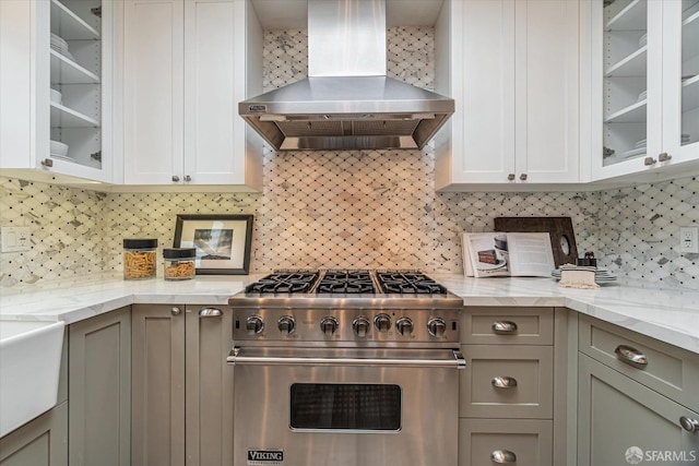 kitchen featuring wall chimney range hood, premium stove, glass insert cabinets, and gray cabinetry