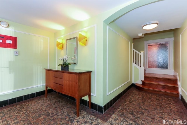 hallway with stairway, arched walkways, and baseboards