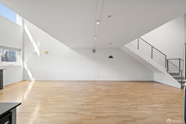 additional living space featuring stairway, light wood-style flooring, and a towering ceiling