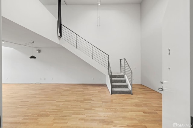 unfurnished living room with stairs, a towering ceiling, and wood finished floors