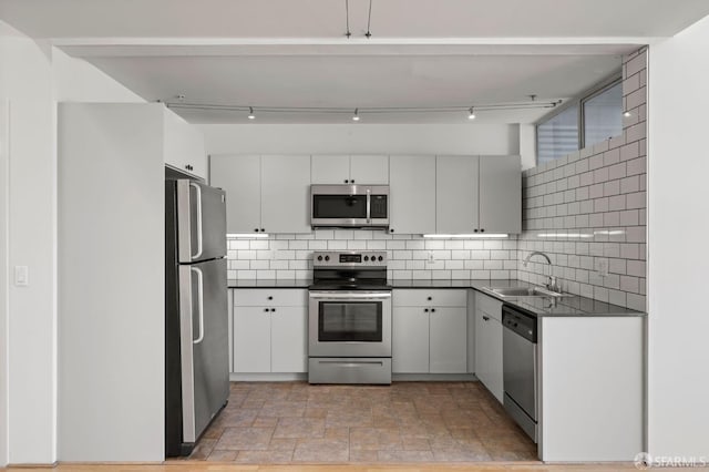 kitchen with a sink, stone finish flooring, dark countertops, appliances with stainless steel finishes, and decorative backsplash