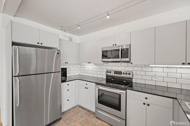 kitchen featuring decorative backsplash, appliances with stainless steel finishes, stone finish flooring, white cabinetry, and dark countertops