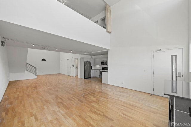 unfurnished living room featuring light wood-style floors, a high ceiling, and rail lighting