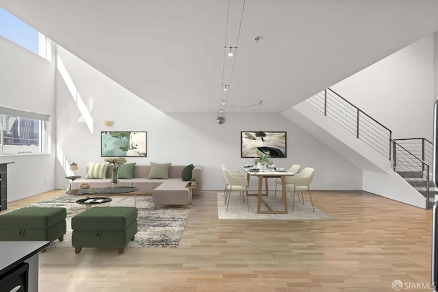 living room featuring a towering ceiling, plenty of natural light, wood finished floors, and stairs