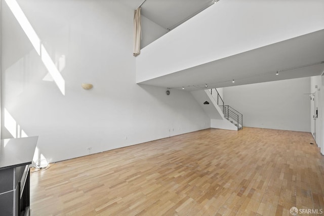 unfurnished living room featuring stairs, a high ceiling, and light wood-style floors