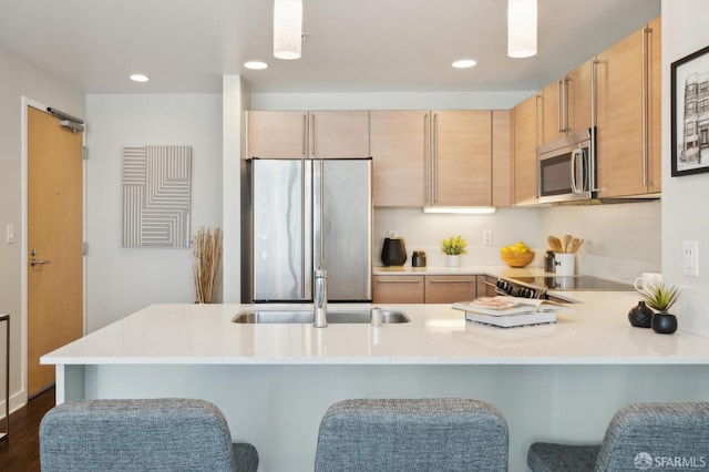 kitchen featuring appliances with stainless steel finishes, light brown cabinetry, decorative light fixtures, sink, and kitchen peninsula