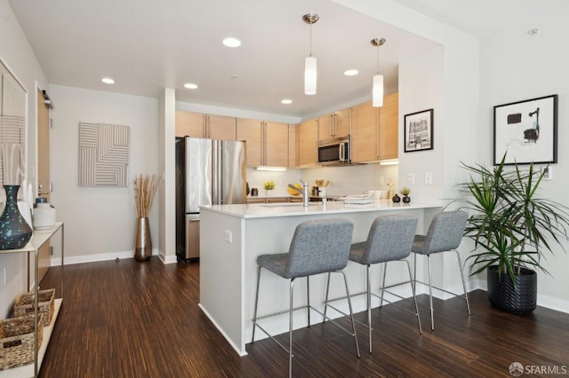 kitchen featuring appliances with stainless steel finishes, light brown cabinetry, decorative light fixtures, kitchen peninsula, and dark wood-type flooring