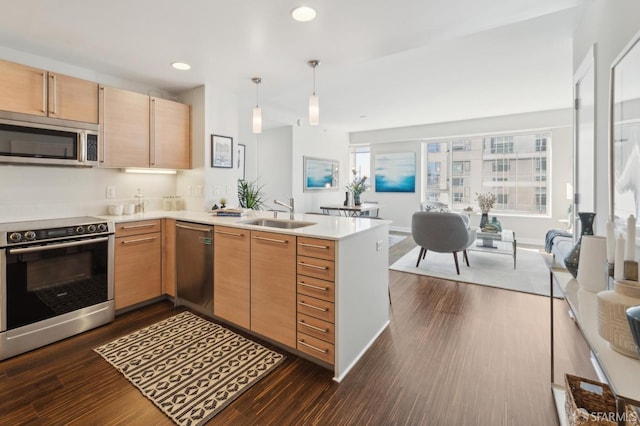 kitchen with appliances with stainless steel finishes, light brown cabinetry, sink, hanging light fixtures, and kitchen peninsula