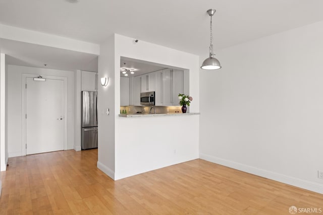 kitchen featuring baseboards, light wood-style floors, appliances with stainless steel finishes, and hanging light fixtures