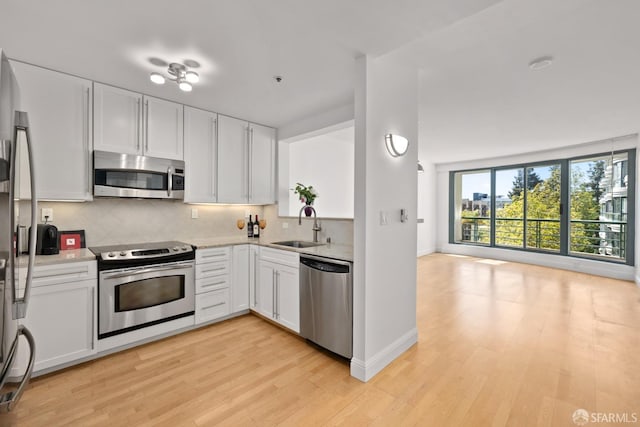 kitchen with backsplash, stainless steel appliances, light wood-style floors, and a sink