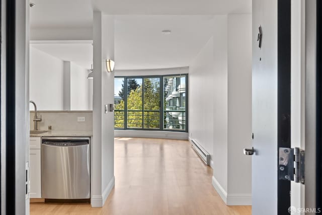hallway featuring light wood-style floors, baseboards, baseboard heating, and a sink