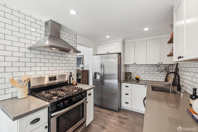 kitchen featuring open shelves, light wood-style flooring, appliances with stainless steel finishes, wall chimney exhaust hood, and a sink