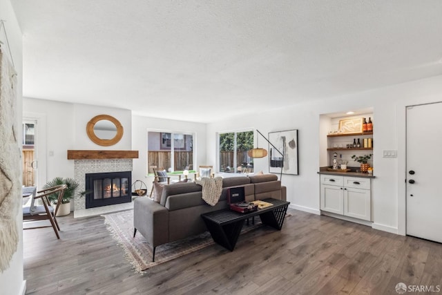 living area featuring a tiled fireplace, a textured ceiling, baseboards, and wood finished floors