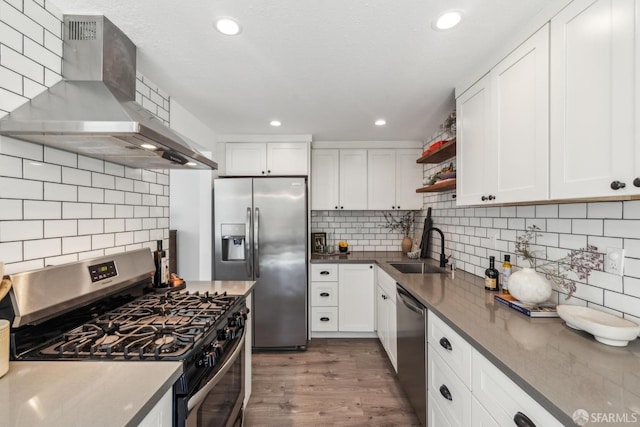 kitchen featuring a sink, open shelves, wood finished floors, appliances with stainless steel finishes, and wall chimney range hood