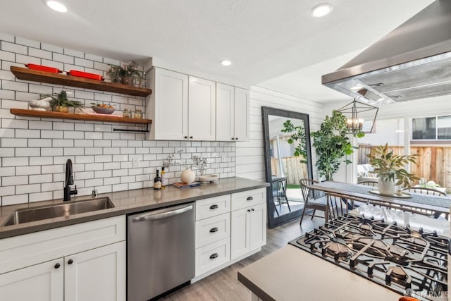 kitchen featuring a sink, cooktop, light wood-style floors, stainless steel dishwasher, and wall chimney exhaust hood