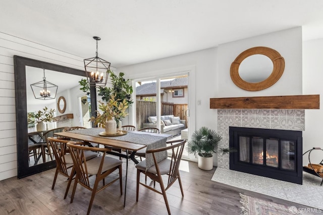 dining space featuring a tiled fireplace, an inviting chandelier, and wood finished floors