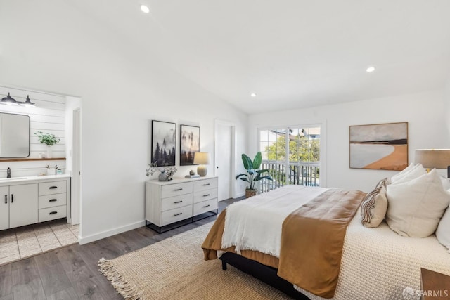 bedroom with wood finished floors, baseboards, ensuite bath, a sink, and vaulted ceiling