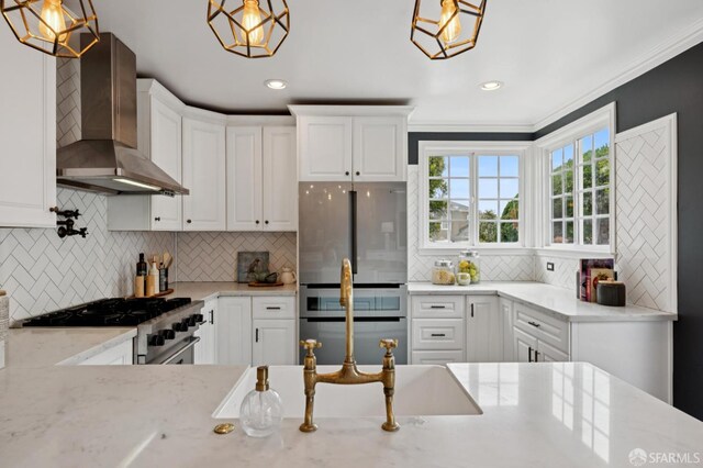 20 Rossmoor Dr, San Francisco, CA 94132 - kitchen featuring wall chimney range hood, appliances with stainless steel finishes, backsplash, white cabinetry, and pendant lighting