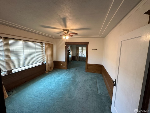 carpeted empty room featuring ornamental molding, wood walls, ceiling fan, and a textured ceiling