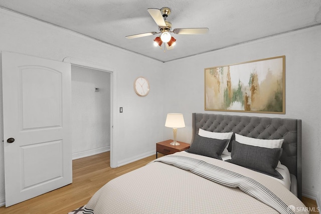 bedroom featuring light wood-style flooring, a textured ceiling, baseboards, and ceiling fan