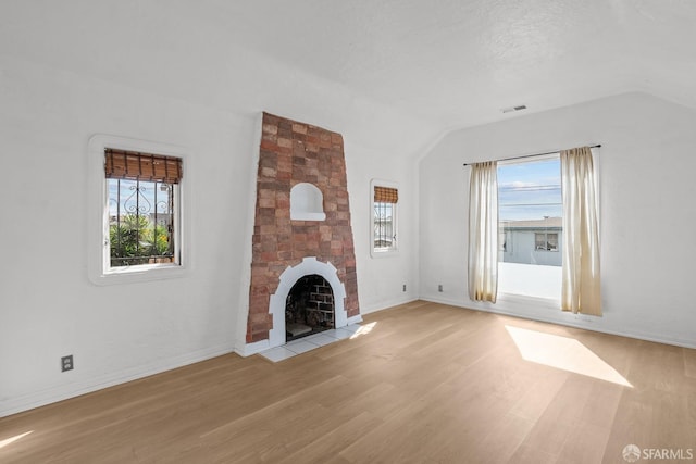 unfurnished living room featuring a fireplace, baseboards, light wood-style floors, and vaulted ceiling