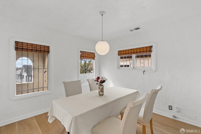 dining space featuring visible vents, baseboards, wood finished floors, and a textured wall