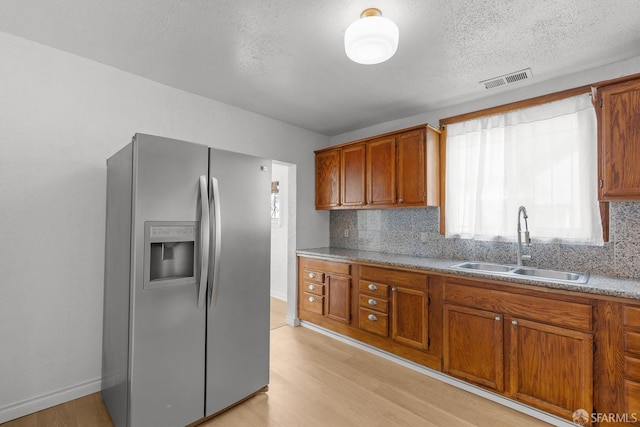 kitchen with brown cabinetry, stainless steel fridge, light wood finished floors, and a sink