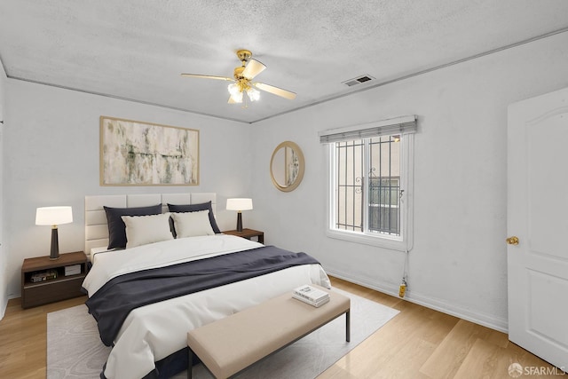 bedroom with visible vents, baseboards, light wood-style flooring, ceiling fan, and a textured ceiling