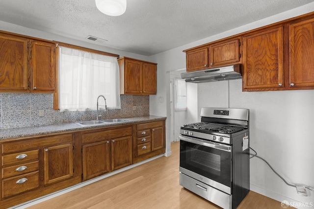 kitchen featuring brown cabinets, under cabinet range hood, a sink, light wood-style floors, and gas range