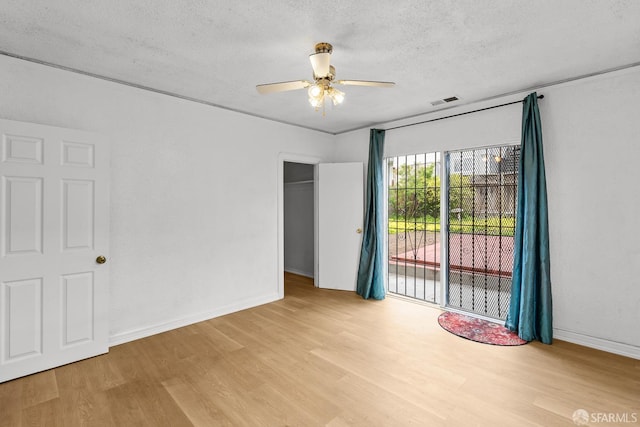 spare room featuring visible vents, baseboards, wood finished floors, a textured ceiling, and a ceiling fan