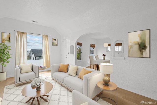 living room with wood finished floors, visible vents, baseboards, arched walkways, and a textured wall